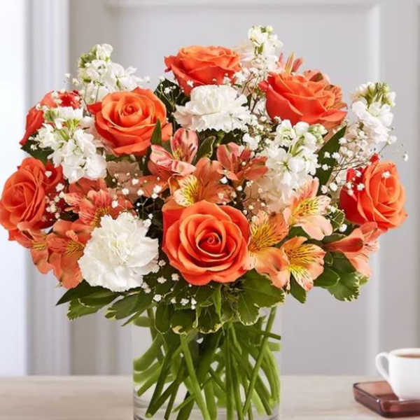 Orange roses and white flowers arranged in a clear glass vase