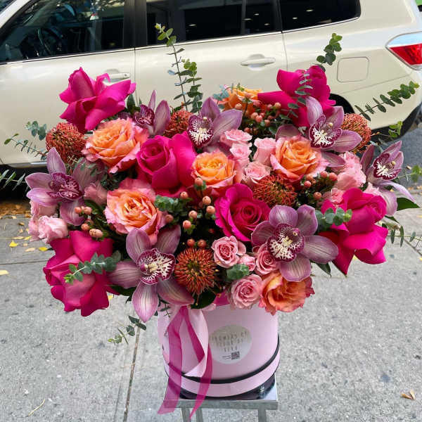 Pink and peach roses with purple orchids in a pink hatbox