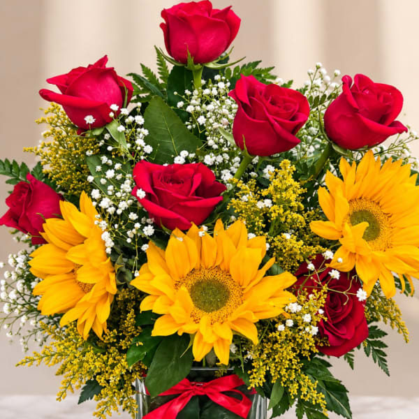 Red roses and yellow sunflowers in a glass vase with baby's breath
