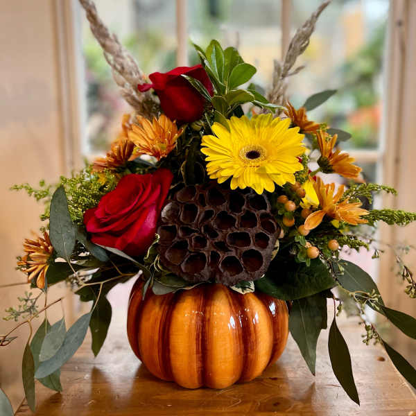 Autumn floral arrangement in a pumpkin container with red roses and yellow daisies