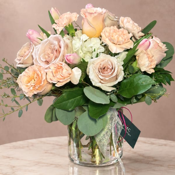 Peach and blush roses with carnations in a clear glass vase