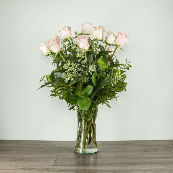 Pink roses in a clear glass vase with mixed greenery