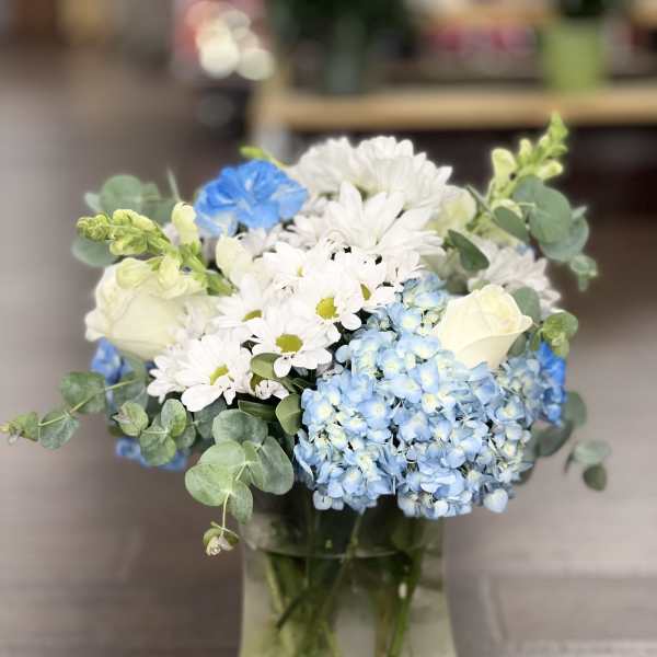 Blue hydrangeas and white daisies with roses in a glass vase