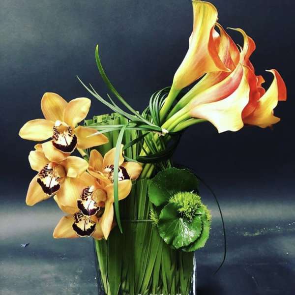 Orange calla lilies and orchids arranged in a clear glass vase