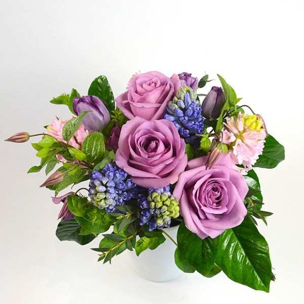 Lavender roses with purple tulips and blue flowers in a white vase