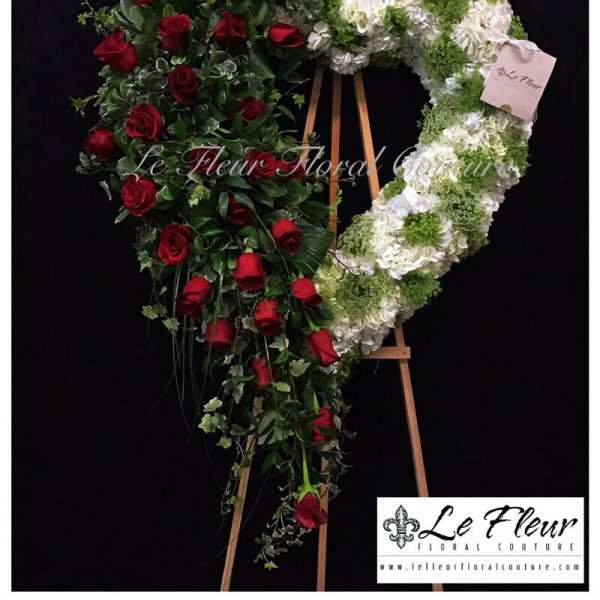 Heart-shaped floral wreath with red roses and white-green blooms on an easel