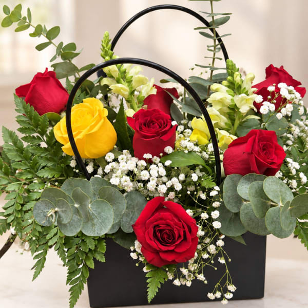 Red and yellow roses arranged in a black handled box with white filler flowers