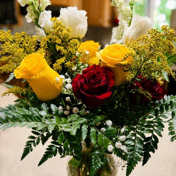 Bouquet of red and yellow roses with white flowers in a glass vase