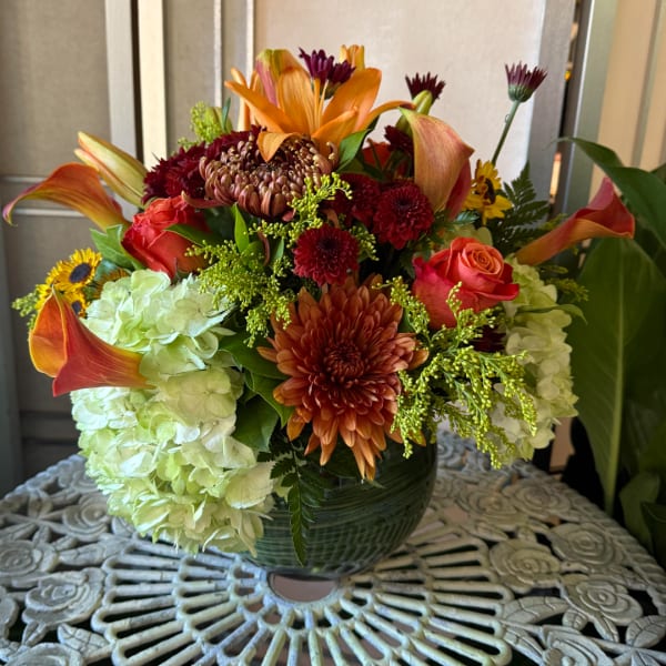 Mixed bouquet with orange lilies, roses, chrysanthemums, and pale hydrangeas in a green vase