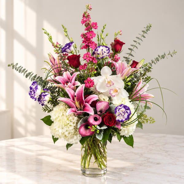 Mixed bouquet of pink lilies, roses, orchids, and white hydrangeas in a glass vase