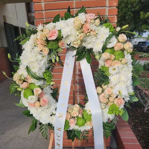 Standing wreath of white mums and peach roses with ribbon on wooden easel