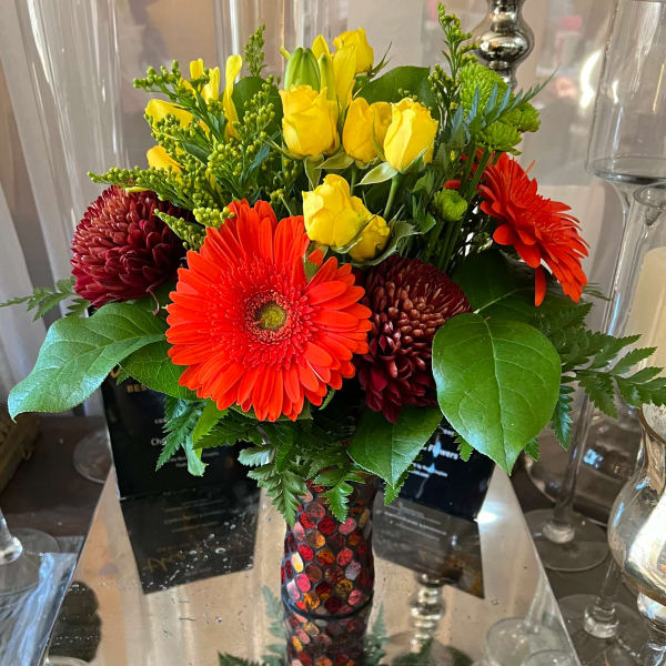 Bright bouquet of yellow roses and red gerbera daisies in a mosaic vase