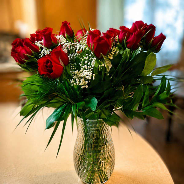 Red roses arranged in a clear glass vase with white filler flowers
