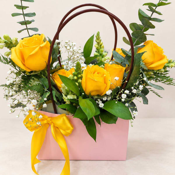 Yellow roses arranged in a pink gift bag with a ribbon bow