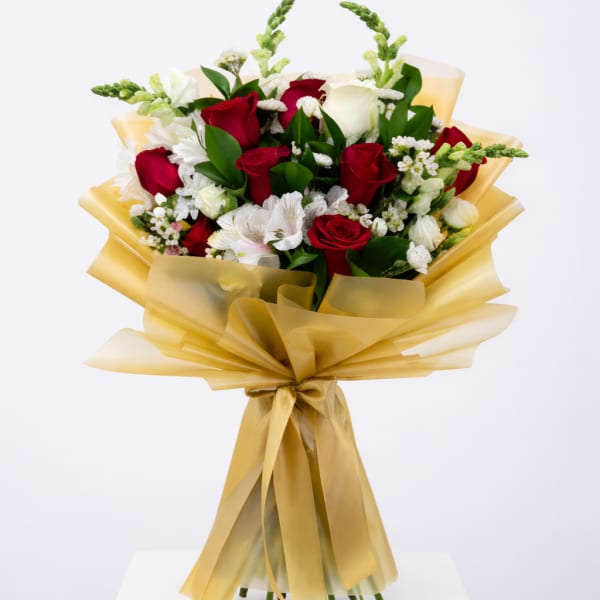 Hand-tied bouquet of red and white roses with white accent flowers wrapped in gold cellophane and ribbon.