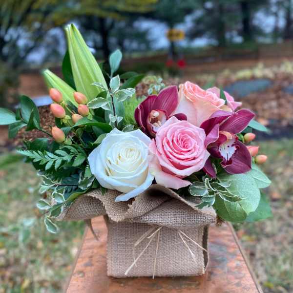 Pink and white roses with purple orchids in a burlap-wrapped box