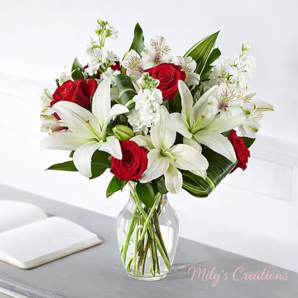 Red roses and white lilies with curled green leaves arranged in a clear glass vase