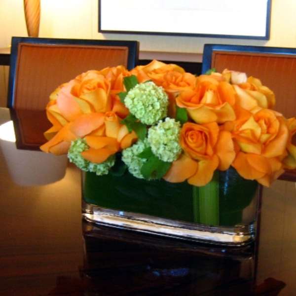 Orange roses arranged in a square glass vase with green blooms