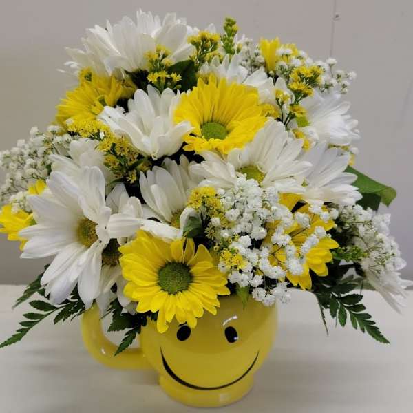 Yellow and white daisy bouquet in a smiley-face mug