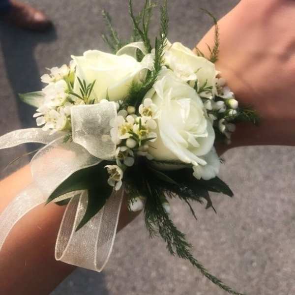 White rose wrist corsage with small white blooms and sheer ribbon on a person's wrist