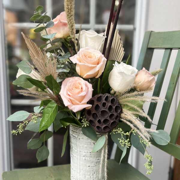 Peach and white roses with dried accents in a tall white ceramic vase