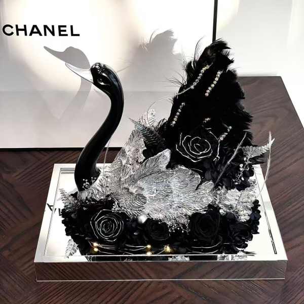 Black floral arrangement with a swan figurine in a mirrored tray