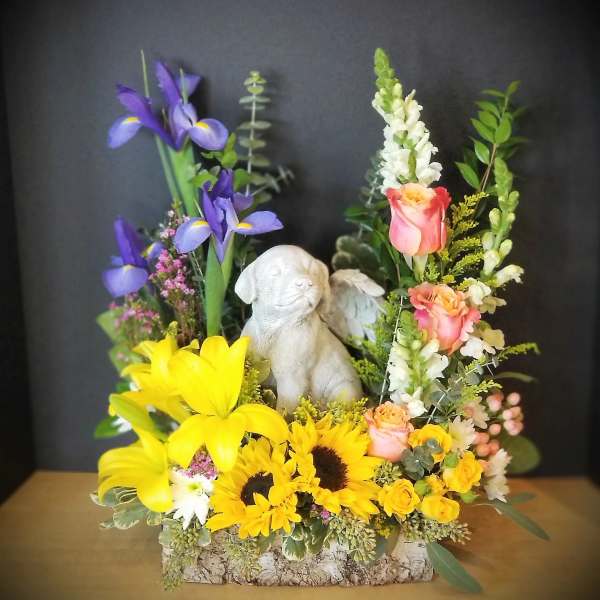 Colorful floral arrangement with a small dog figurine in a bark-textured container