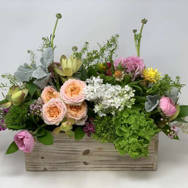 Low garden-style arrangement of mixed pastel flowers in a rustic wooden box