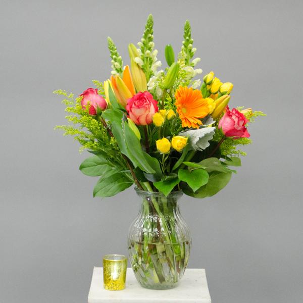 Mixed bouquet of pink, yellow, and orange flowers in a glass vase