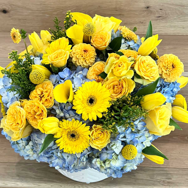 Yellow flowers and blue hydrangeas arranged in a white vase