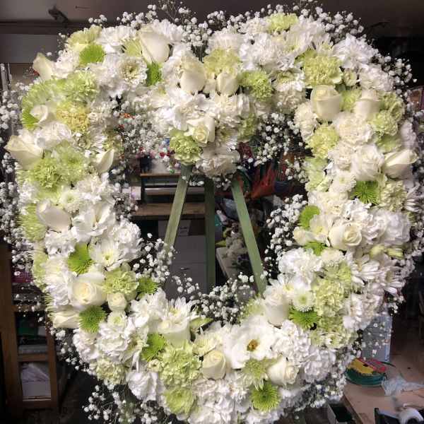 Heart-shaped floral wreath of white and pale green flowers on an easel