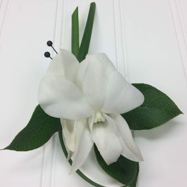 White orchid corsage with green leaves and black berry accents