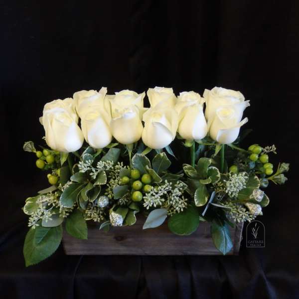 White roses arranged in a wooden box with green berries and foliage