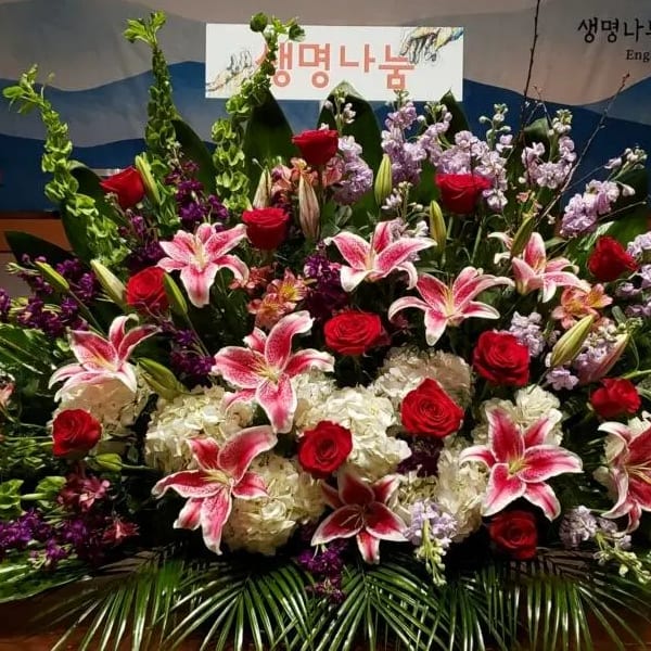 Large altar-style arrangement with pink lilies, red roses, white hydrangeas, and purple flowers