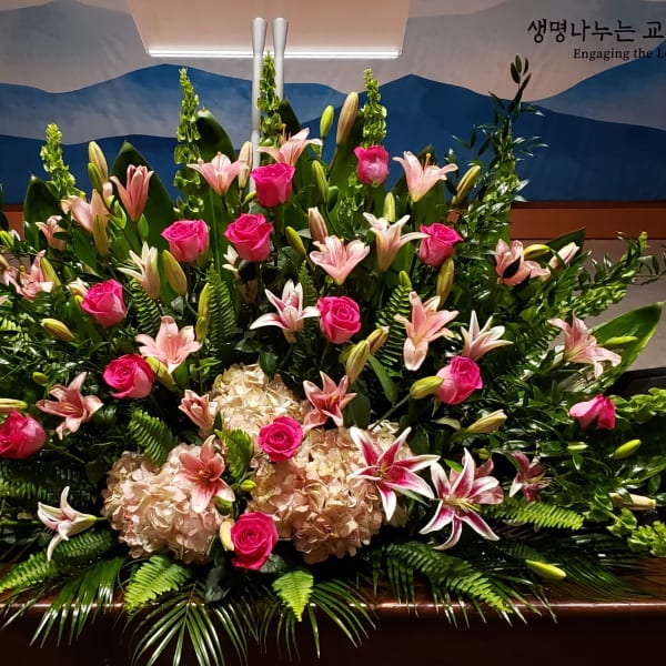 Large fan-shaped arrangement of pink roses, lilies, and hydrangeas on a stage backdrop