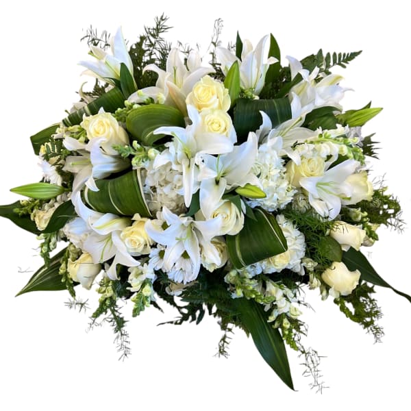 White lilies and roses arranged in a low bouquet with dark green foliage