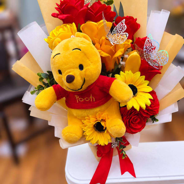 Winnie the Pooh plush surrounded by red and yellow flowers in a wrapped bouquet
