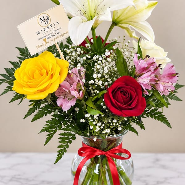 Mixed bouquet of roses and lilies in a glass vase with a red ribbon