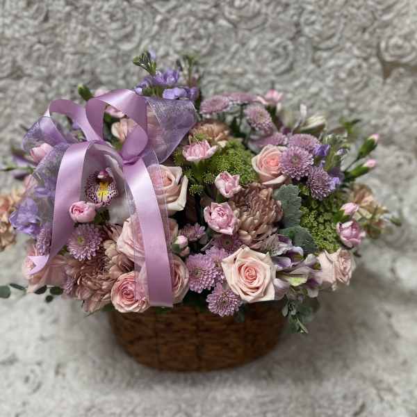 Basket arrangement of pink and lavender flowers with a purple ribbon