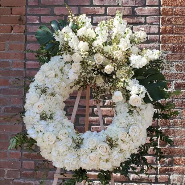 Large white floral wreath on a wooden easel against a brick wall