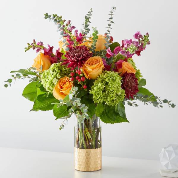Bouquet of orange roses, green hydrangeas, and burgundy blooms in a glass vase
