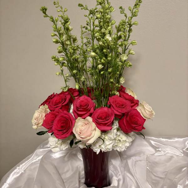 Tall bouquet of red, pink, and white roses in a burgundy vase