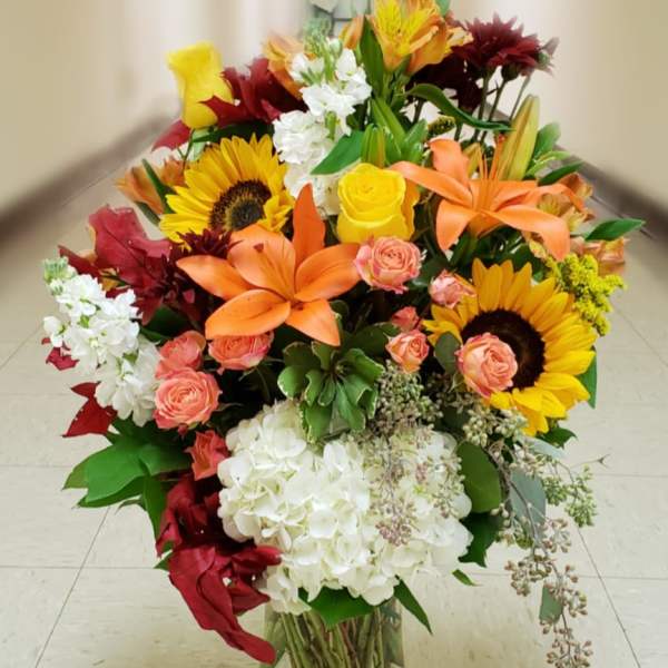 Large mixed bouquet with sunflowers, lilies, roses, and white hydrangeas in a glass vase