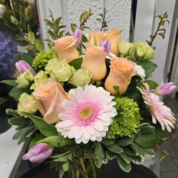 Bouquet of peach roses, pink gerbera daisies, and purple tulips in a glass vase