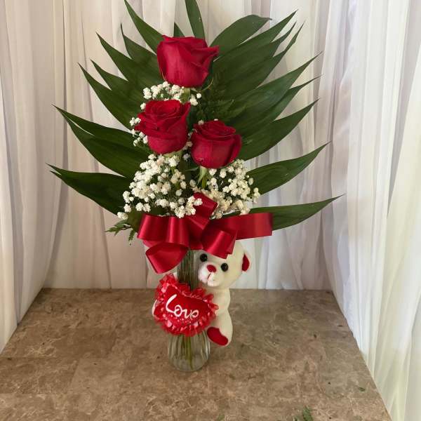 Red roses in a glass vase with a teddy bear and love ribbon