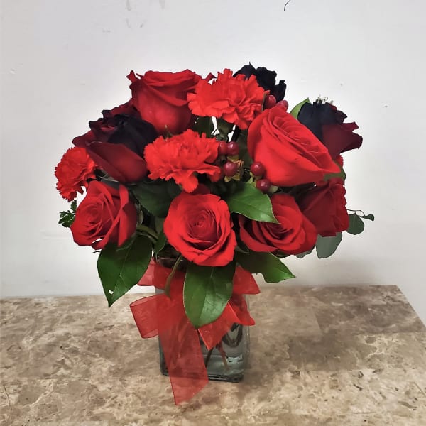 Red roses and carnations arranged in a glass vase with a red ribbon.