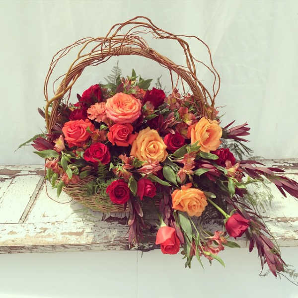 Basket arrangement of orange and red roses with mixed foliage