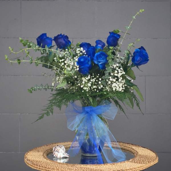 Blue roses in a glass vase with white baby's breath and a blue ribbon