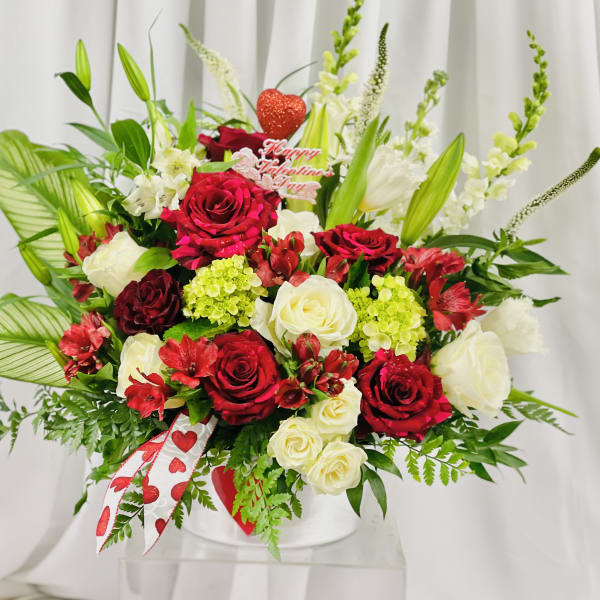 Red and white rose arrangement in a white vase with a Valentine topper