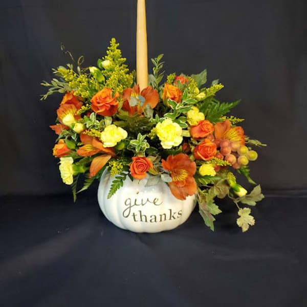 Orange and yellow floral arrangement in a white pumpkin container with a candle